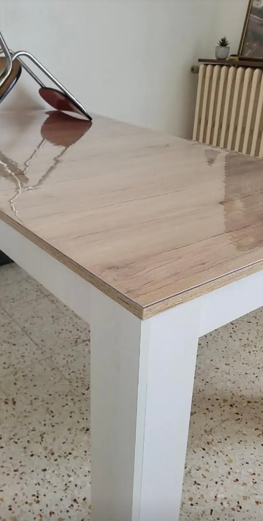 Helle Tischplatte auf weißen Beinen mit dem Glanz der Matte; im Hintergrund ein gusseiserner Heizkörper