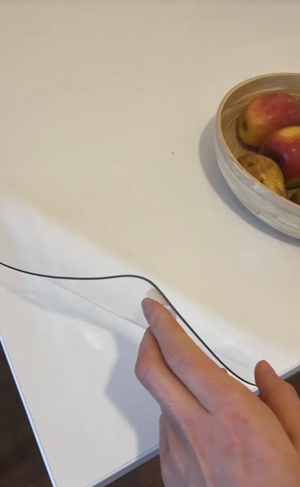 Weiße Platte mit einer Schale Äpfel und Birnen; eine Hand streicht den Rand der transparenten Auflage glatt