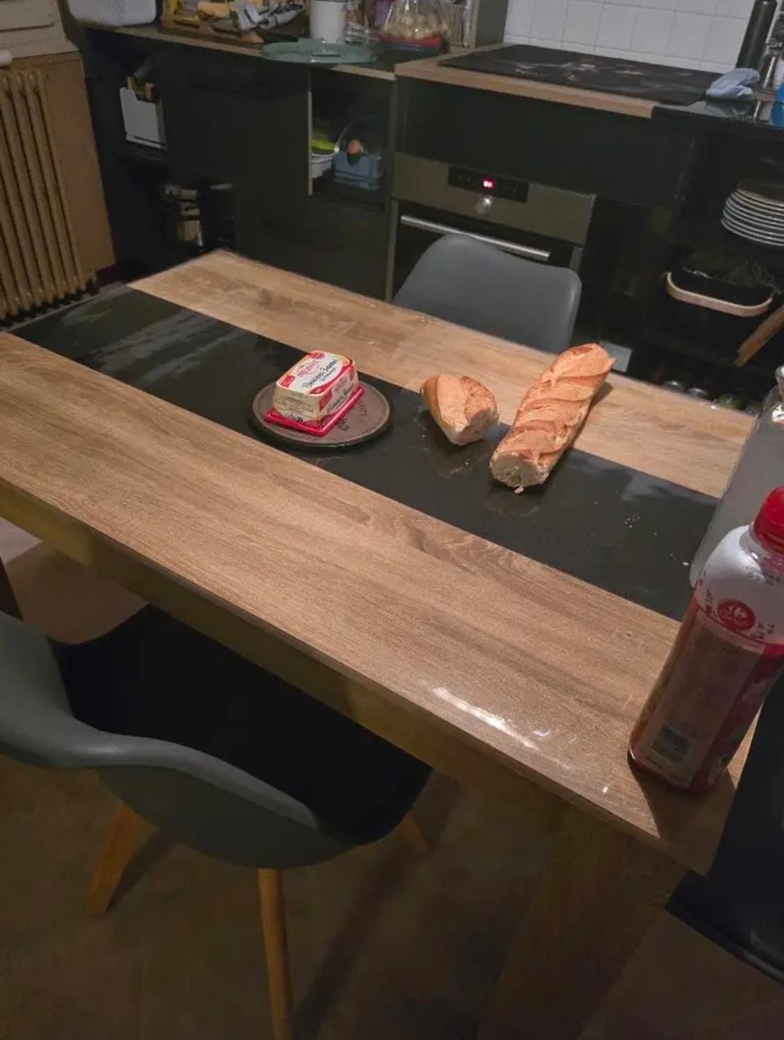 Küchentisch mit dunklem Streifen in der Mitte, darauf Baguette und Butter; die Platte unter weichem Glas