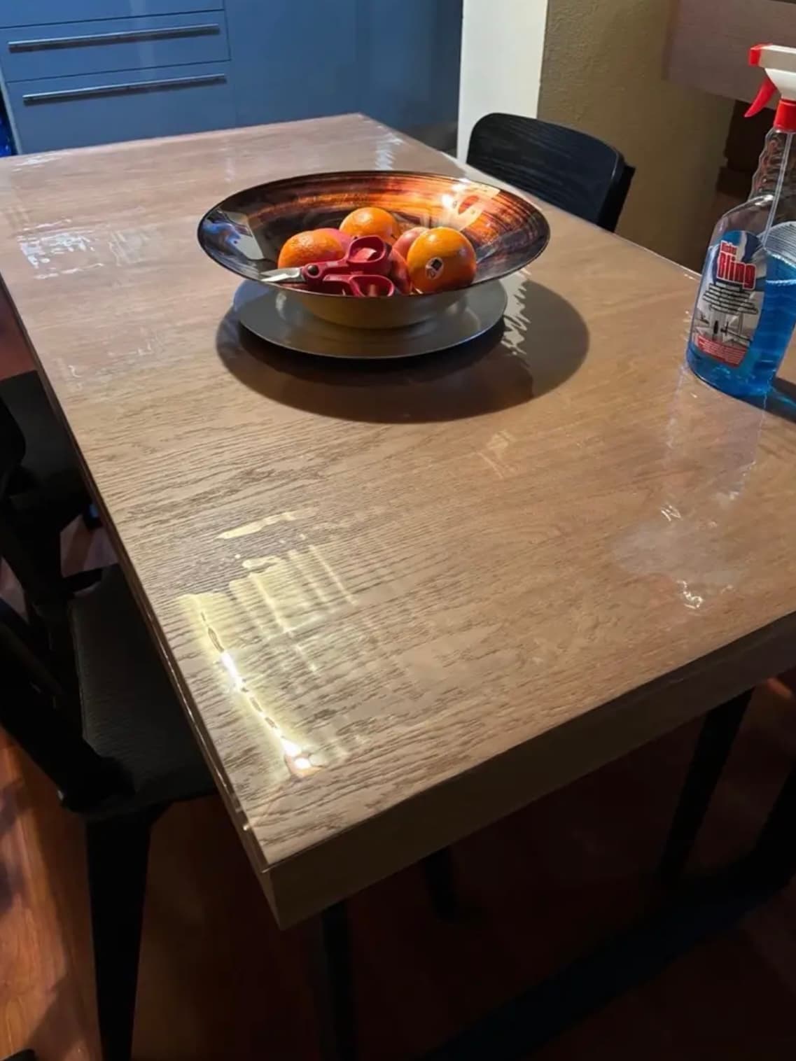 Metallschale mit Orangen auf einer Eichenplatte; neben der Matte steht eine Flasche Glasreiniger