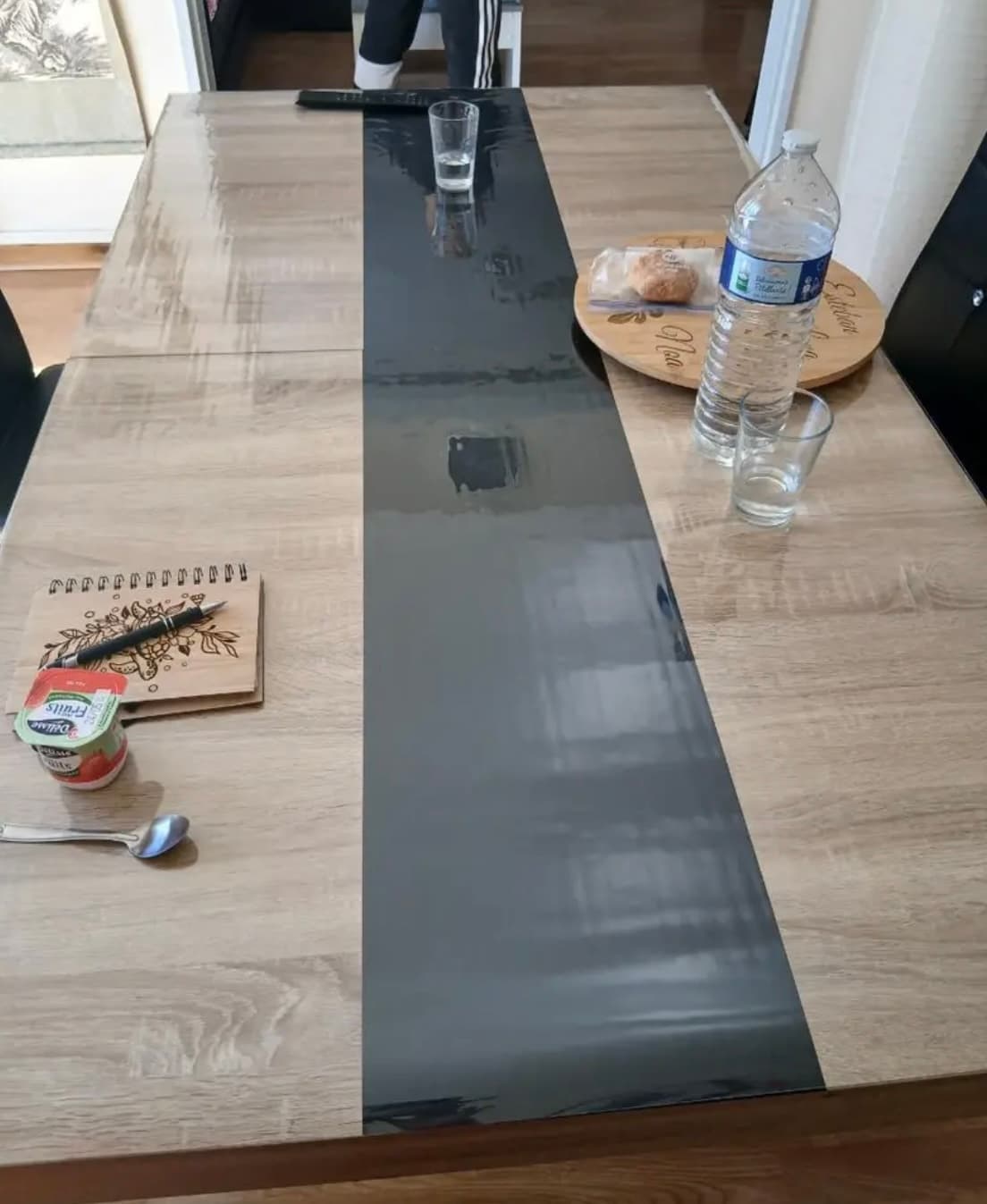 Frühstück auf einem langen Tisch mit graphitfarbenem Streifen: Wasser, Gläser, Notizbuch — alles auf der Matte
