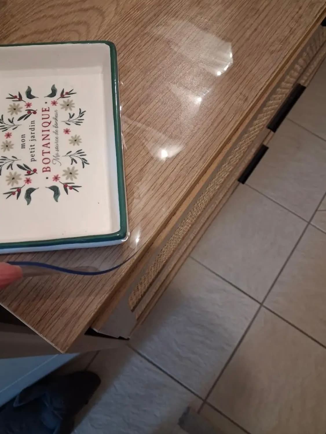 Ecke einer Eichenkommode mit dekorativem Tablett; eine Hand hält den Rand der transparenten Auflage fest
