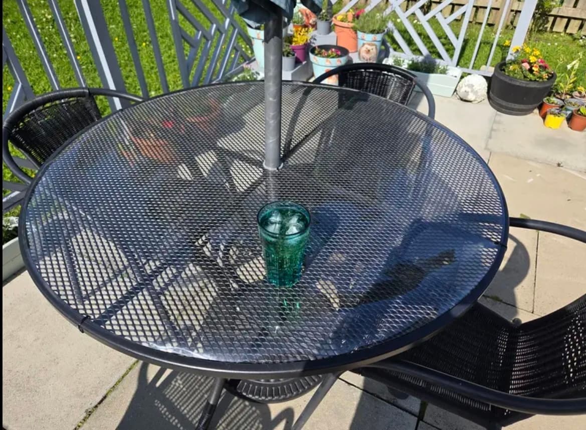 Matte auf einem runden Tisch auf der Terrasse, ein Glas mit Getränk in der Mitte, ringsum Blumentöpfe
