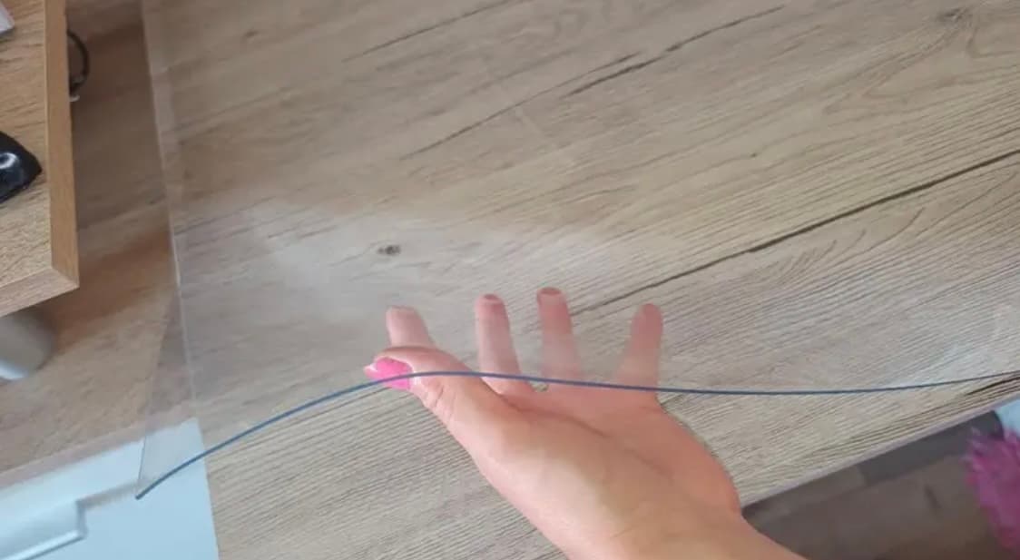 Eine Hand ist unter die transparente Matte geschoben, die auf einer hellen Holzplatte liegt