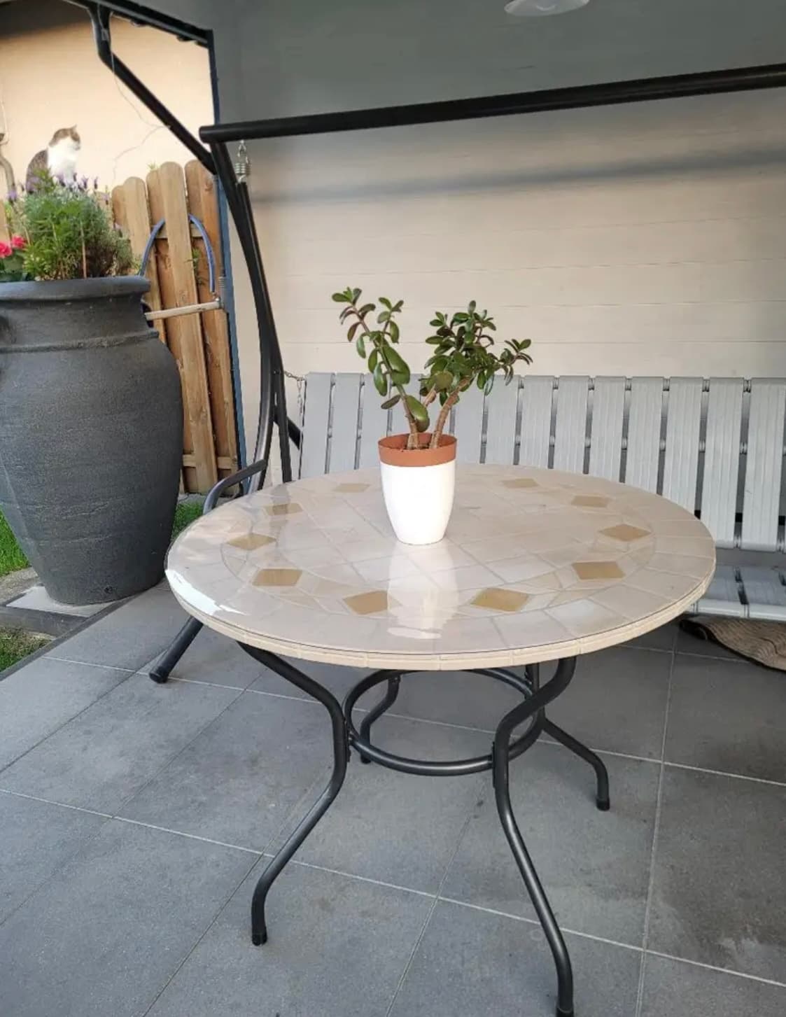 Runder Tisch mit Mosaikplatte auf der Terrasse, auf der Matte ein Topf mit Geldbaum