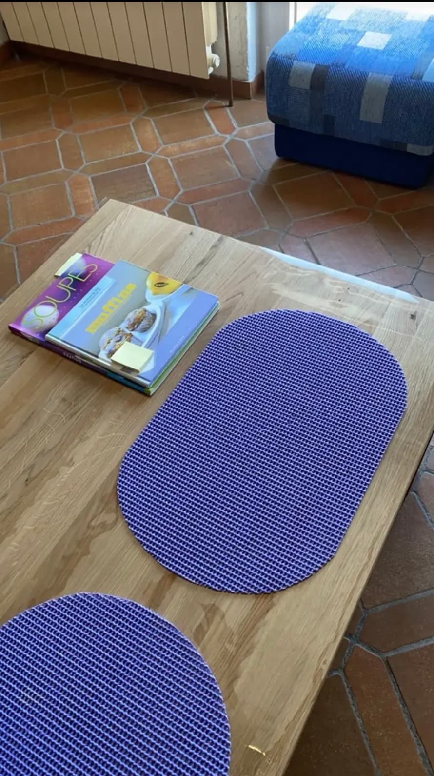 Eichentisch mit violetten Platzsets und Kochbüchern; der Rand der Matte ragt über die Platte hinaus