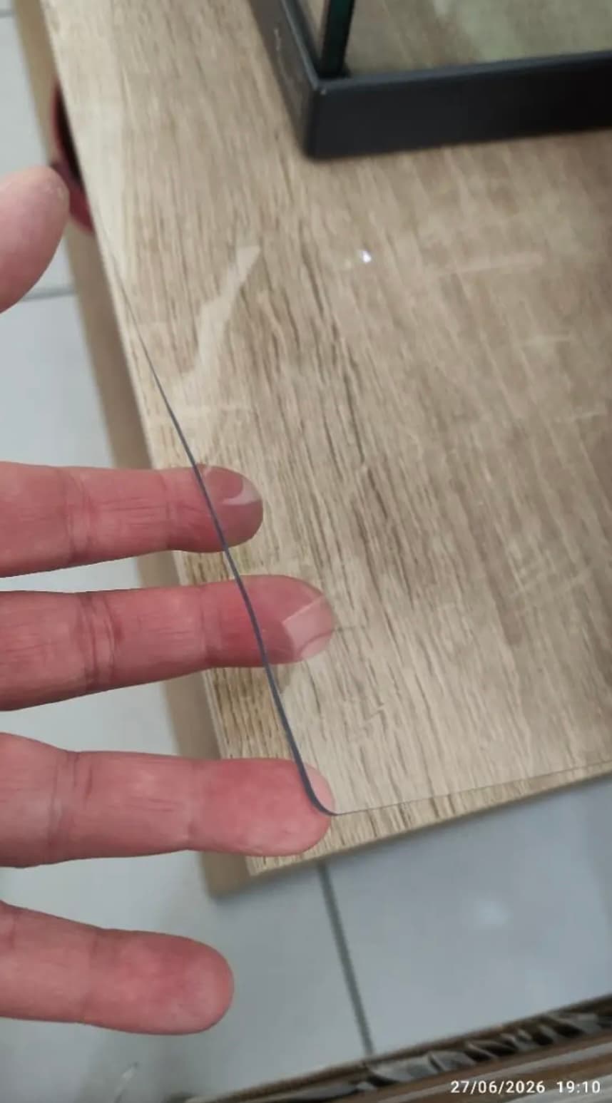 Finger halten die Ecke der Matte auf einer Eichenplatte — im Gegenlicht sieht man die Stärke des Materials