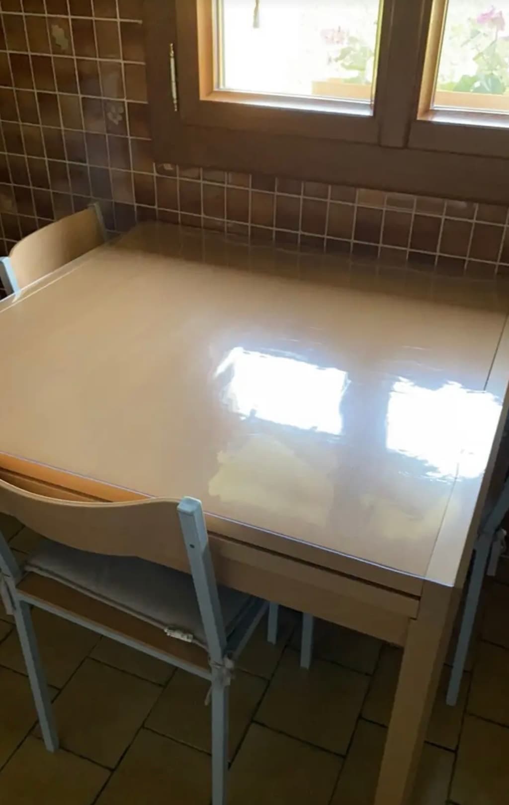 Kleiner cremefarbener Tisch in einer gefliesten Küche; auf der Platte die Matte, im Fenster Töpfe mit Geranien