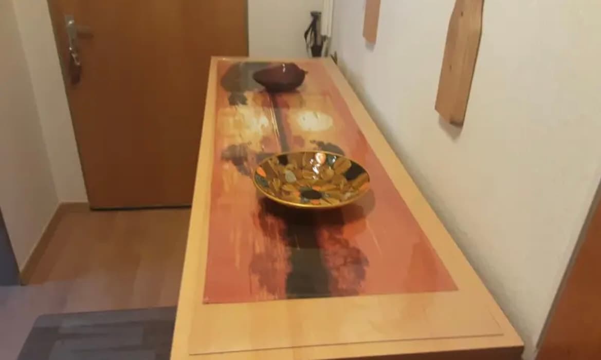 Schmaler heller Tisch im Flur: unter der Matte ein rotes Muster der Platte, obenauf eine Messingschale