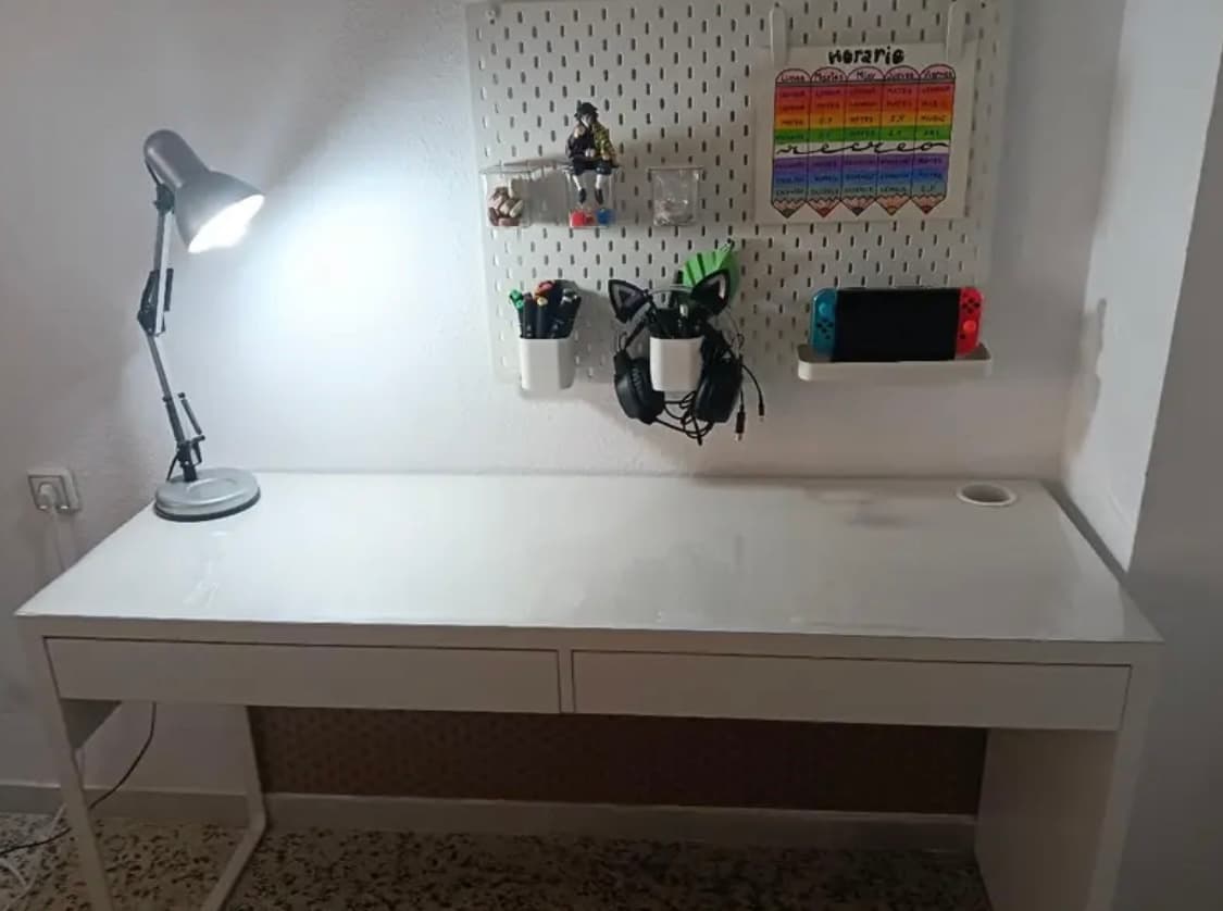 Weißer Schreibtisch mit Lampe und Werkzeugwand; die Platte schützt eine transparente Auflage