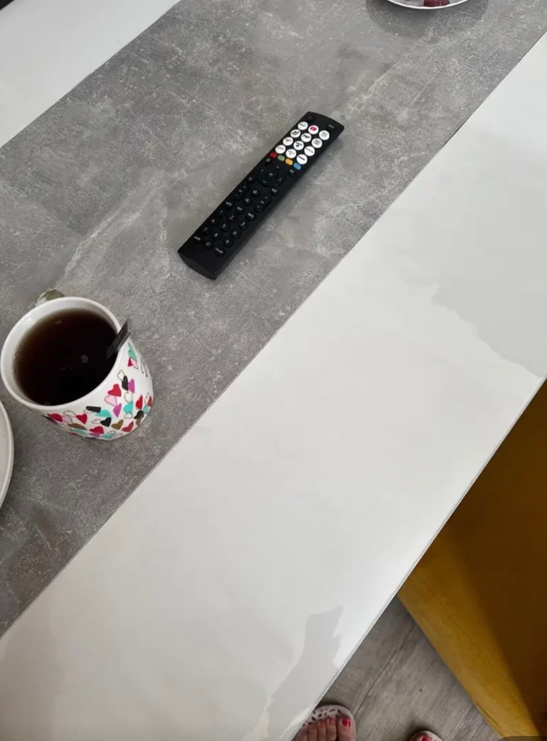 Tisch mit weißer Platte und grauem Betonstreifen: Teetasse und Fernbedienung liegen auf der Matte